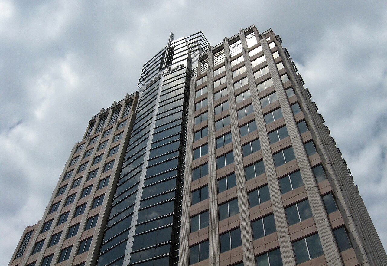 Looking up at a tall office tower under a cloudy sky, with the Accenture name near its top.
