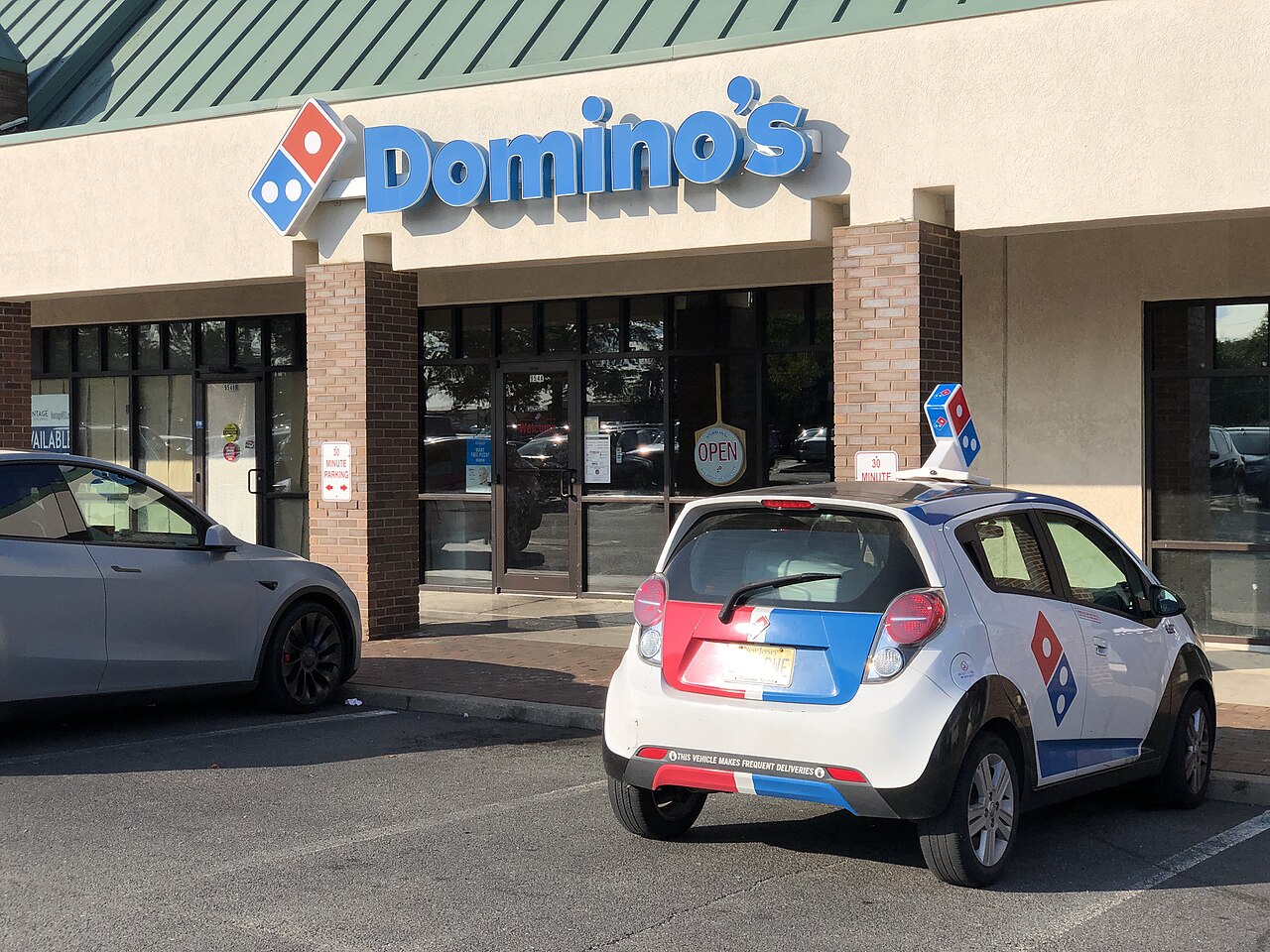 A Domino's Pizza storefront in a shopping center, with a branded delivery car parked outside
