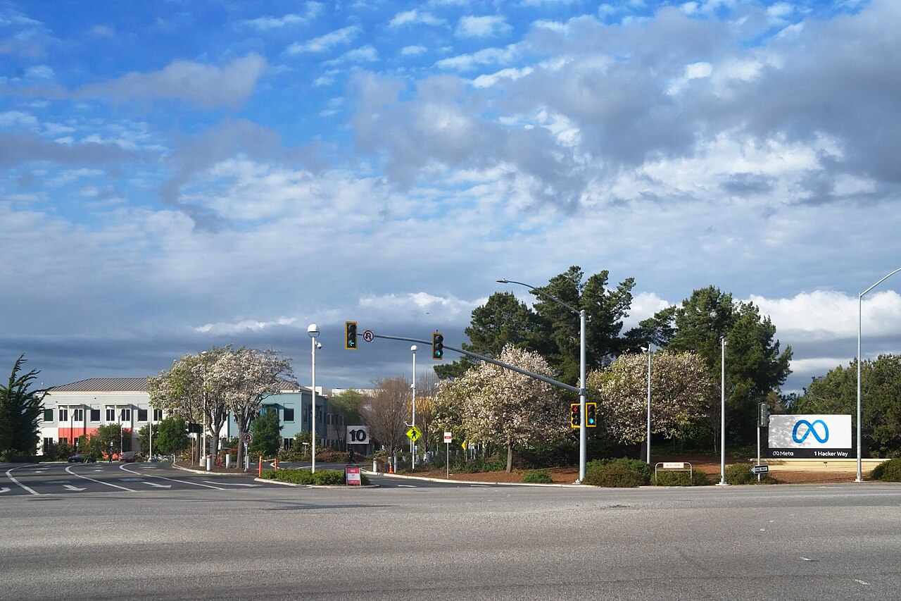A road junction with traffic lights, trees and a Meta sign at the entrance to an office campus