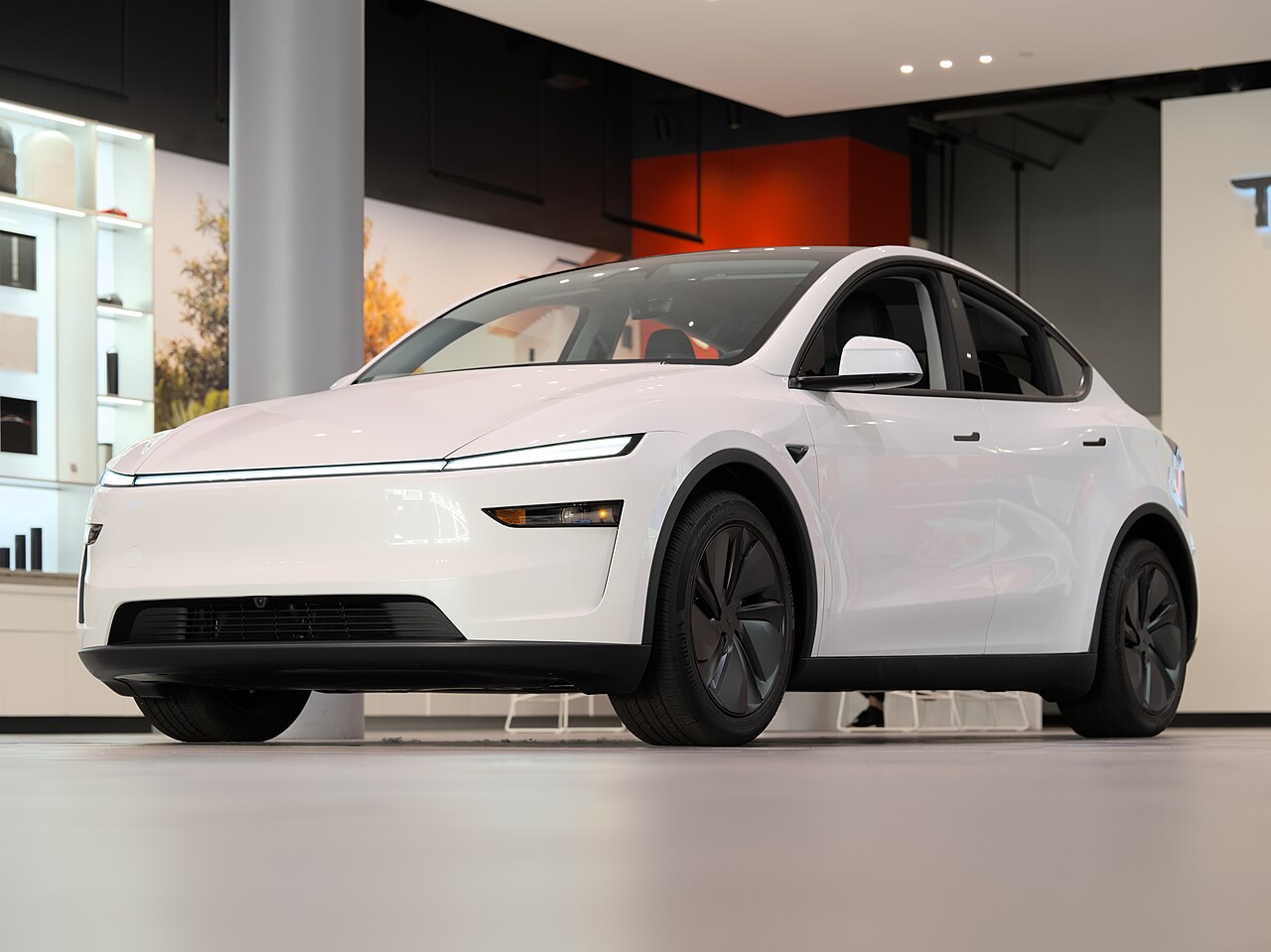 A white Tesla Model Y crossover on a showroom floor, seen from the front at an angle