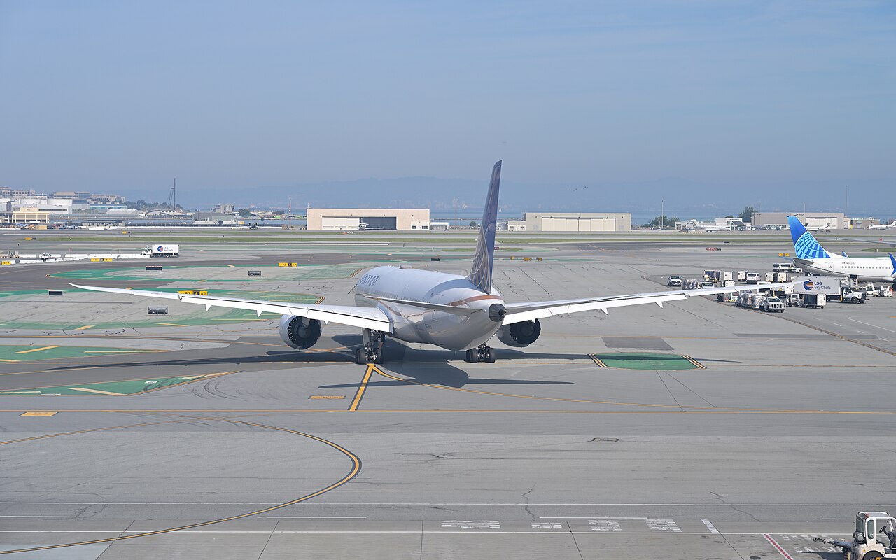 A United Airlines Boeing 787-9 seen from behind as it taxis on an airport apron, with another United jet at a gate on the right